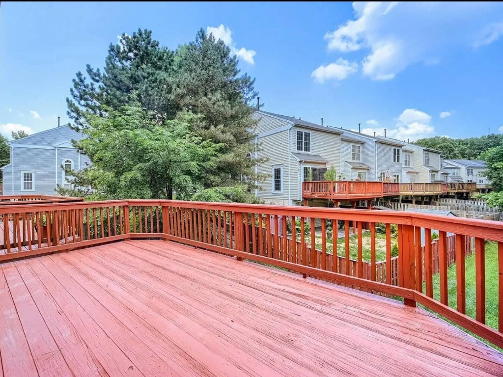 Wooden deck with railing overlooking a tree-lined neighborhood.
