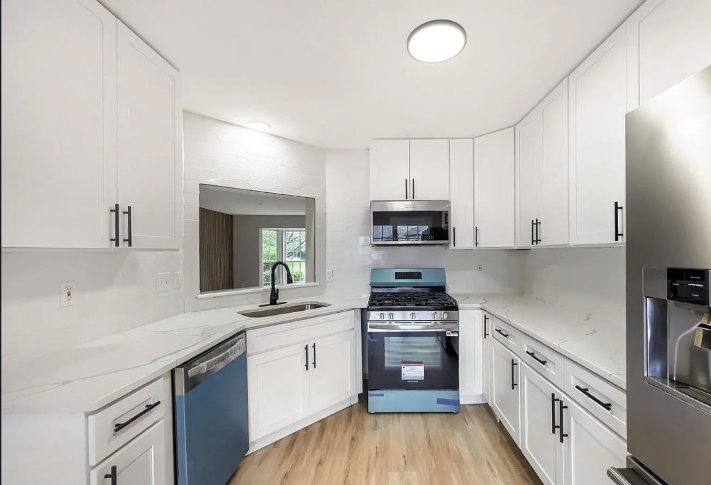 Modern white kitchen remodel with marble-style countertops and stainless steel appliances.