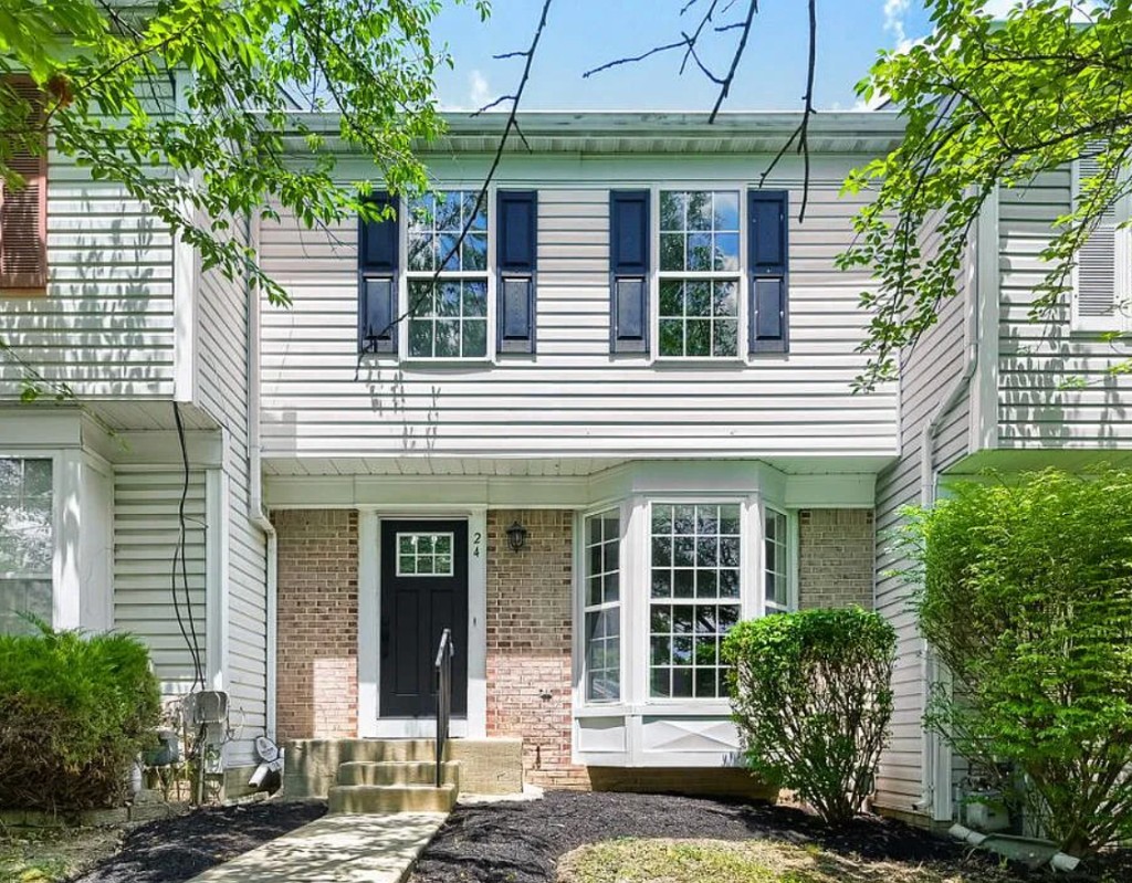 Townhouse exterior with light siding, brick accents, and black shutters.